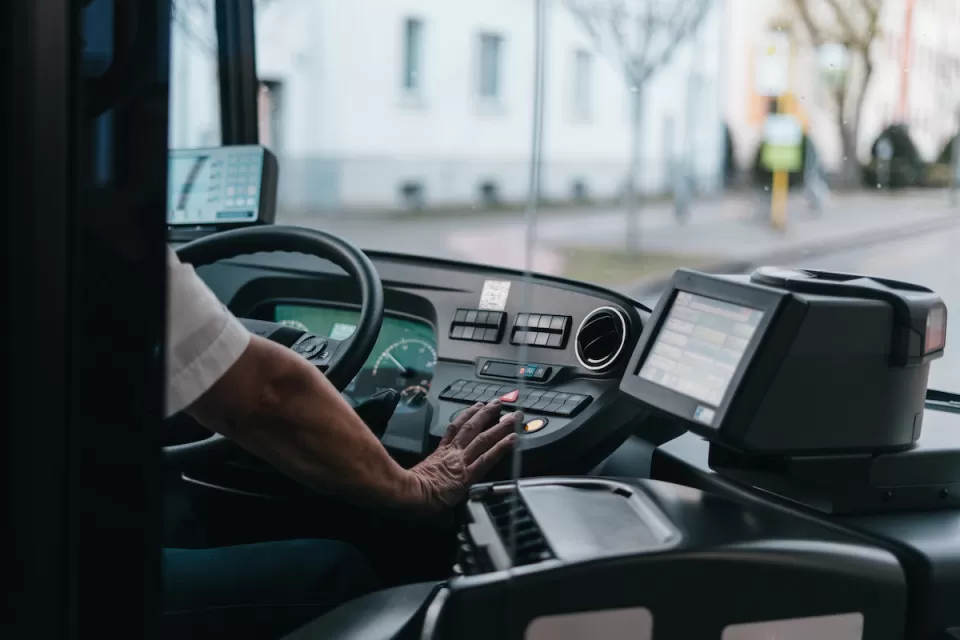 Close-up of bus driver from behind with only hand visible on steering wheel.